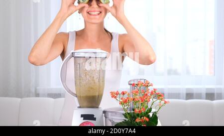 Glückliche junge Frau bereitet leckere nahrhafte Smoothie im Mixer. Lustige Frau macht Augen aus Kiwi. Stockfoto