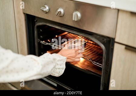 Frau trägt Ofenhandschuh Putting Backblech mit rohen Cookies In modernen Backofen in der heimischen Küche Stockfoto