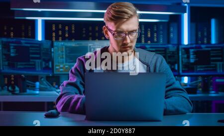 Portrait des Software-Entwicklers Hacker Gamer trägt Brille und Headset sitzt an seinem Schreibtisch und arbeitet auf Laptop spielen. Im Hintergrund dunkel hoch Stockfoto