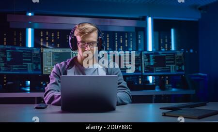 Portrait des Software-Entwicklers Hacker Gamer trägt Brille und Headset sitzt an seinem Schreibtisch und arbeitet auf Laptop spielen. Im Hintergrund Dunkles Neon Stockfoto
