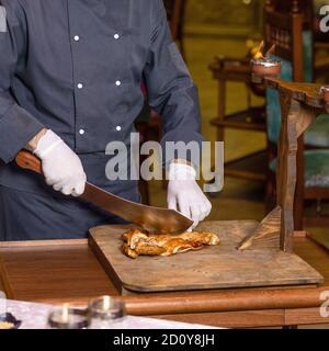 Koch schneidet ein Hühnerfleisch mit einem Spaltmesser auf dem Holzplatte Stockfoto