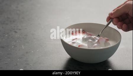 Mann Hand essen Schokolade Müsli mit Erdbeeren und Joghurt auf einer Betonplatte, breites Foto Stockfoto