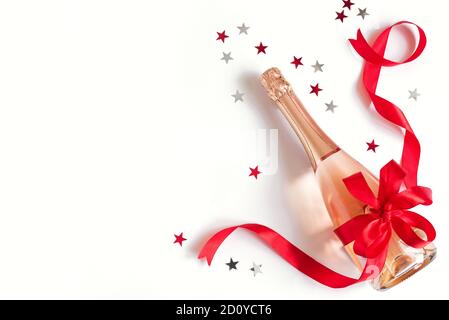 Champagnerflasche mit roter Schleife und Sternen isoliert auf weißem Hintergrund. Campagne für Weihnachten oder Geburtstag, Draufsicht, Kopierbereich. Stockfoto