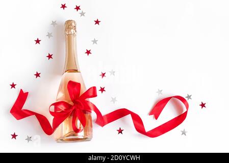Champagnerflasche mit roter Schleife und Sternen isoliert auf weißem Hintergrund. Campagne für Weihnachten oder Geburtstag, Draufsicht, Kopierbereich. Stockfoto