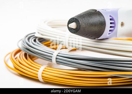 Nahaufnahme der Reihe von bunten gerollten Kabel und Kinder 3D-Druckstift isoliert auf weiß. Drei helle Filament Kunststoff liegen drinnen. Konzept Stockfoto
