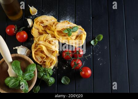 Italienische Pasta. Lockige Pappardella Pasta, Tomaten, frisches Basilikum und Knoblauch auf dunklem Hintergrund. Blick von oben. Stockfoto