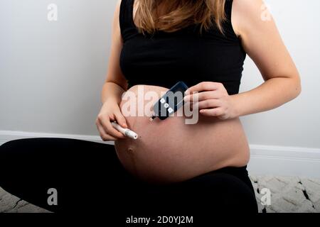 Schwangere Frau verifing glykämischen Index mit Gerät für Schwangerschaftsdiabetes in der Schwangerschaft. Zuckerfreie Ernährung und gesunde Ernährung Konzept Lebensstil für NOR Stockfoto