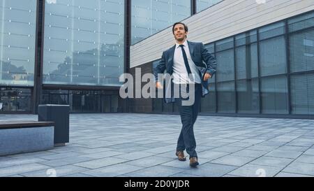 Fröhlicher und glücklicher Geschäftsmann in einem Anzug ist aktiv Tanzen auf einem Street Square. Szene aufgenommen in einem städtischen Betonpark neben dem Business Center. Sonnig Stockfoto