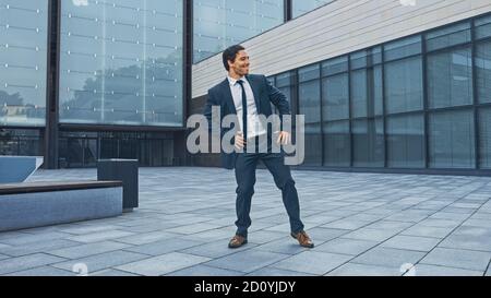 Fröhlicher und glücklicher Geschäftsmann in einem Anzug ist aktiv Tanzen auf einem Street Square. Szene aufgenommen in einem städtischen Betonpark neben dem Business Center. Sonnig Stockfoto