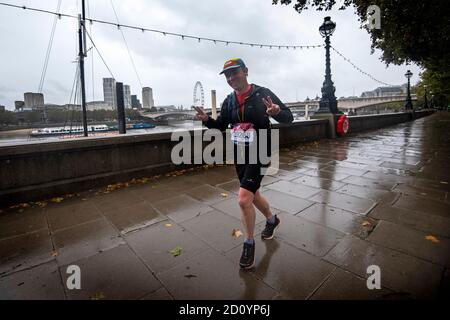 Ein Läufer, der eine London Marathon-Laufnummer auf dem Embankment im Zentrum von London trägt, während etwa 45,000 Menschen den 40. London Marathon auf seiner eigenen 26.2-Meilen-Strecke durch Großbritannien laufen oder laufen, nachdem das ursprünglich für April 26 geplante Ereignis aufgrund eines Coronavirus verschoben wurde. Stockfoto