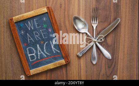 Tafel im Restaurant, die die Wiedereröffnung nach der Corona-Sperre ankündigte, Besteck und Tafel, Essen Business Restart Konzept mit Nachricht wir sind zurück Stockfoto