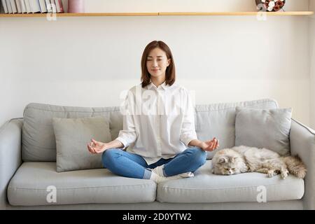 Junge asiatische Frau sitzt auf der Couch zu Hause üben Yoga Stockfoto