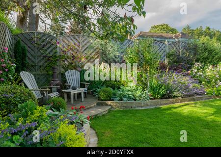 Landschaftlich schöner, sonniger privater Garten (modernes Design, farbenfrohe Sommerblumen, Randpflanzen, Sitzmöbel auf der Terrasse, Rasen) - Yorkshire, England, Großbritannien Stockfoto