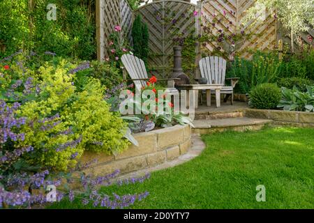 Landschaftlich schöner, sonniger privater Garten (modernes Design, farbenfrohe Sommerblumen, Randpflanzen, Sitzmöbel auf der Terrasse, Rasen) - Yorkshire, England, Großbritannien Stockfoto