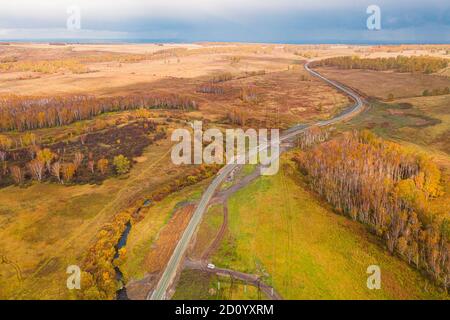 Luftaufnahme auf Eisenbahn im Bau, zwischen Wäldern, Feldern und Dörfern. Straßenarbeiten im Wald und auf Feldern. Unbefestigte Straße in einem offenen Bereich Stockfoto