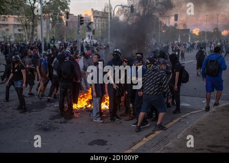 Santiago, Chile. Oktober 2020. Demonstranten wärmen ihre Körper durch ein Feuer in der Nähe des Autos startet Wasser der Bereitschaftspolizei.Hunderte von Demonstranten konfrontieren die Polizei in der Nähe der Plaza Baquedano, von den Menschen umbenannt 'Plaza de la Dignidad', um Gerechtigkeit für Antoni zu fordern, Eine 16-Jährige, die am vorigen Protesttag von der Polizei von einer Brücke geworfen wurde. Kredit: SOPA Images Limited/Alamy Live Nachrichten Stockfoto