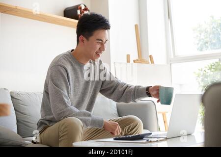 Glücklich und lächelnd junge asiatische Geschäftsführer von zu Hause aus arbeiten Vorschlagen eines Toasts während eines Meetings mit Kollegen oder Kunden mit Videoanruf Stockfoto