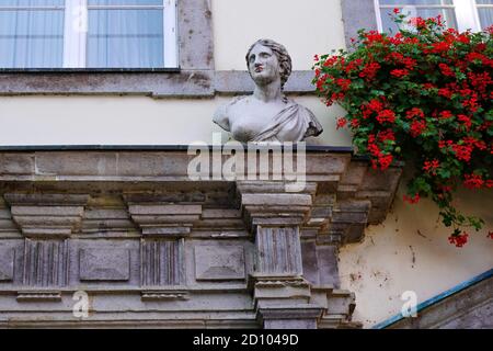 Architektonisches Detail eines alten Gebäudes in der Düsseldorfer Altstadt mit dekorativer Steinfigur und roten Blumen. Stockfoto