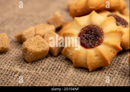 Hausgemachte Gebäck Cookies mit Marmelade und Stücke von braunem Rohrzucker auf einem Hintergrund von homespun Stoff mit einer rauen Textur, Nahaufnahme, selektive Fokus Stockfoto