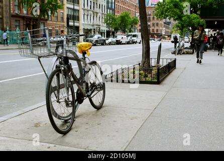 NEW YORK, USA - 10. MAI 2019: Fahrrad an einen Stand in der West 14th Street in der Innenstadt von New York City am 10. Mai 2019 gekettet. Fußgänger gehen entlang der sid Stockfoto