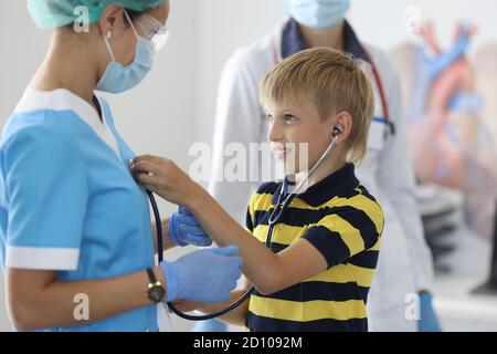 Junge im gestreiften T-Shirt mit schwarzem Stethoskop dem Herzschlag des Arztes zuhören. Stockfoto