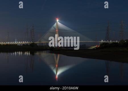 Die Flintshire Bridge, die nachts beleuchtet ist und den Fluss Dee vom Connah's Quay aus überspannt, ist mit Kabelgestellen ausgestattet. Fächerartige Struktur, die sich in der gespiegelten Mündung widerspiegelt Stockfoto