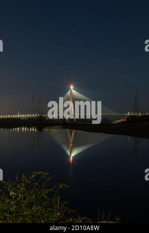 Die Flintshire Bridge, die nachts beleuchtet ist und den Fluss Dee vom Connah's Quay aus überspannt, ist mit Kabelgestellen ausgestattet. Fächerartige Struktur, die sich in der gespiegelten Mündung widerspiegelt Stockfoto