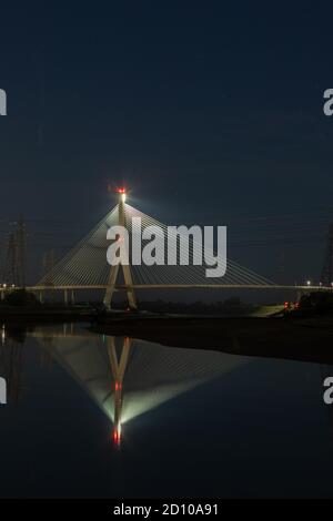 Die Flintshire Bridge, die nachts beleuchtet ist und den Fluss Dee vom Connah's Quay aus überspannt, ist mit Kabelgestellen ausgestattet. Fächerartige Struktur, die sich in der gespiegelten Mündung widerspiegelt Stockfoto