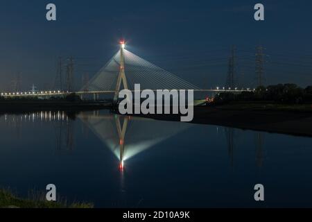 Die Flintshire Bridge, die nachts beleuchtet ist und den Fluss Dee vom Connah's Quay aus überspannt, ist mit Kabelgestellen ausgestattet. Fächerartige Struktur, die sich in der gespiegelten Mündung widerspiegelt Stockfoto