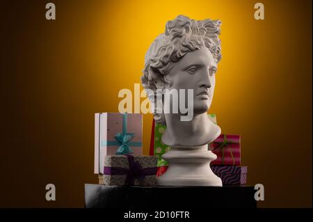 Weiße Gipsstatue von Apollo Belvedere, Geschenkboxen und Verpackungen, in blauem Konturlicht auf mehrfarbigem Hintergrund. Stockfoto