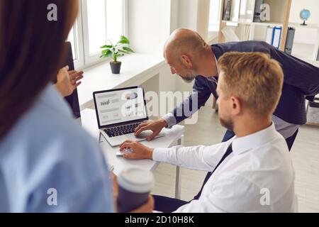 Mitarbeiter analysieren Datenstatistiken auf einem Laptop, indem sie auf einen Bildschirm zeigen, auf dem Grafiken und Diagramme angezeigt werden. Stockfoto