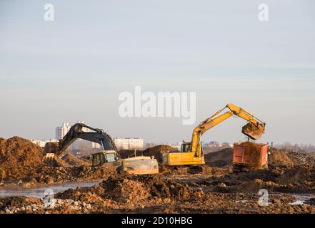 Bagger auf einer Baustelle graben den Boden für das Fundament und verlegen Sturmabwasserkanäle. Straßenarbeiten. Kleine Rauheitsschärfe, mögliche Granula Stockfoto