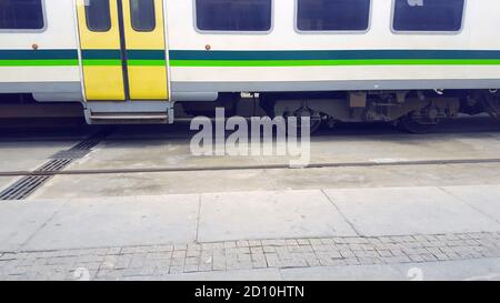 Angehobene Personenzugwagen, LKW auf dem Bahnhof, Bahnhof, Bahnhof oder Depot. Weißer Zug mit farbigen grünen und gelben Linie Stockfoto