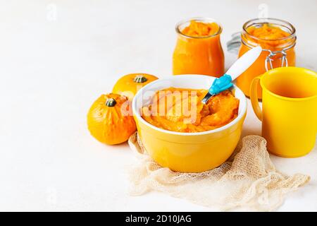 Hausgemachtes Kürbispüree in Schüssel mit Babylöffel und frischen Kürbissen auf hellem Hintergrund. Das Konzept der Babynahrung. Stockfoto