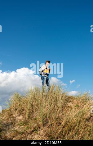 Männlicher Rucksacktourist, der auf einer Sanddüne und Gras vor einem blauen Himmel Hintergrund steht Stockfoto