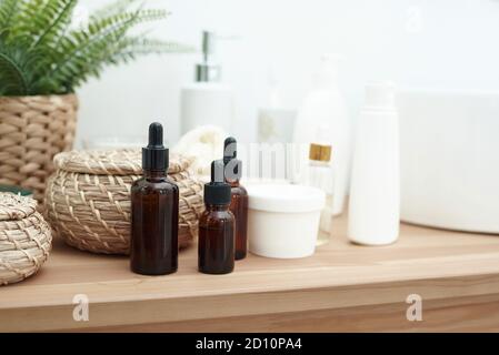 Drei Braunglasflaschen für Serum oder ätherisches Öl auf Holztisch. Braune Tropfflaschen mit natürlicher Bio-Kosmetik. SPA, Hautpflege, Körperbehandlung Konzept. Stockfoto