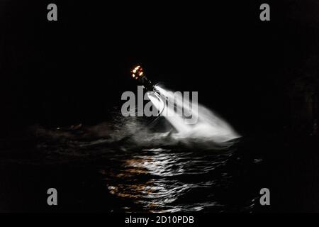 Flyboarding bei Nacht in einem Steinbruch in der Tschechischen Republik. Ein nicht identifizierter Mann führt nachts das Flyboarding durch. Bewegungseffekt, Langzeitbelichtung. Stockfoto