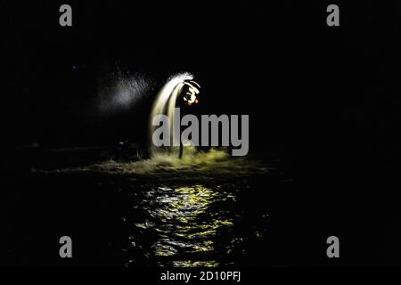 Flyboarding bei Nacht in einem Steinbruch in der Tschechischen Republik. Ein nicht identifizierter Mann führt nachts das Flyboarding durch. Bewegungseffekt, Langzeitbelichtung. Stockfoto