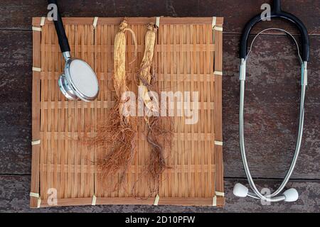 Trockene Ginseng auf schwarze Platte mit Stethoskop auf dem Holz Hintergrund Stockfoto