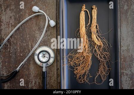 Trockene Ginseng auf schwarze Platte mit Stethoskop auf dem Holz Hintergrund Stockfoto