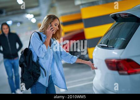 Krimineller Mann in schwarzem Hoodie nähert sich junge Frau Auto öffnen Auf dem Parkplatz Stockfoto