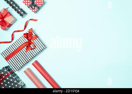 Geschenkschachteln in schwarz-weiß gestreiftem, gepunktetem und rotem Papier mit Verpackungsmaterialien auf blauem Hintergrund. Verschiedene Designs verpackt Geschenke Stockfoto