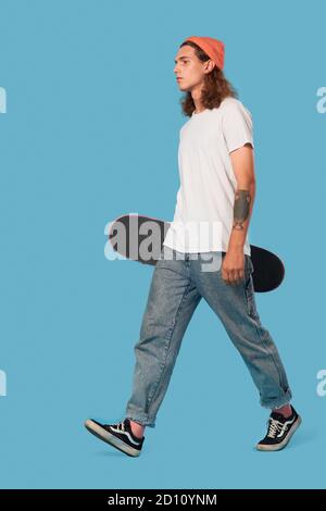 Junge Erwachsene Mann zu Fuß mit Skateboard im Studio Stockfoto