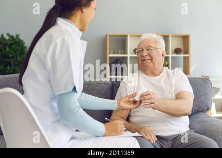 Der junge Arzt besucht ihren älteren Patienten zu Hause, verschreibt Pillen, unterstützt und jubelt ihn an Stockfoto