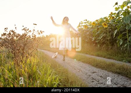 Fröhliche junge Frau in weißem Kleid Spaß beim Bewegen Zwischen Feldern Stockfoto