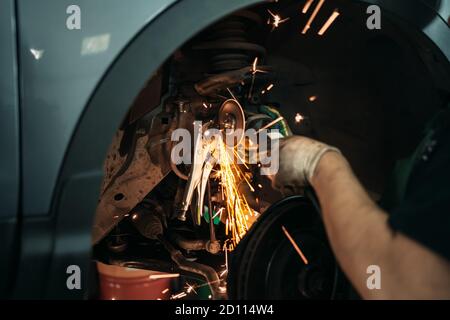 Arbeiter schneidet rostigen Bolzen in der Lenkstange des Autos an der Auto Service Station mit Schleifer, Nahaufnahme. Stockfoto