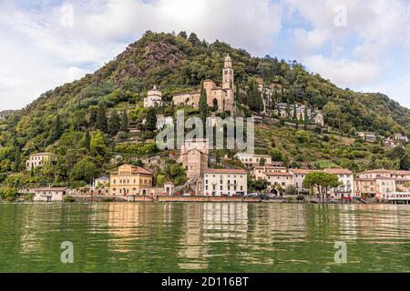 Kulinarische Tour auf dem Luganersee im Tessin, Circolo di Carona, Schweiz. Vom Wasser aus gesehen: Die Kirche Santa Maria del Sasso von Morcote, darunter die historische Altstadt. Viele kleine Restaurants säumen die Uferpromenade Stockfoto