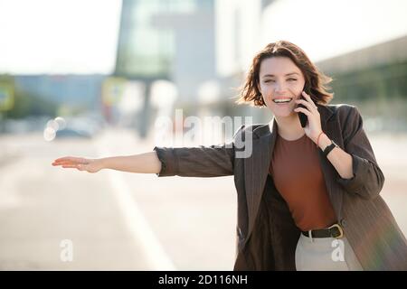 Junge fröhliche Brünette Geschäftsfrau mit Smartphone von Ohr fangen Taxi Stockfoto