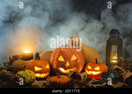 Jack o Laternen auf einem nebligen Hintergrund und mit trockenen Blättern, Kerzen und einigen anderen Kürbissen. Stockfoto