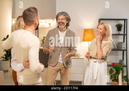 Fröhliche Paare lachen, während sie vor einander stehen Im Wohnzimmer Stockfoto